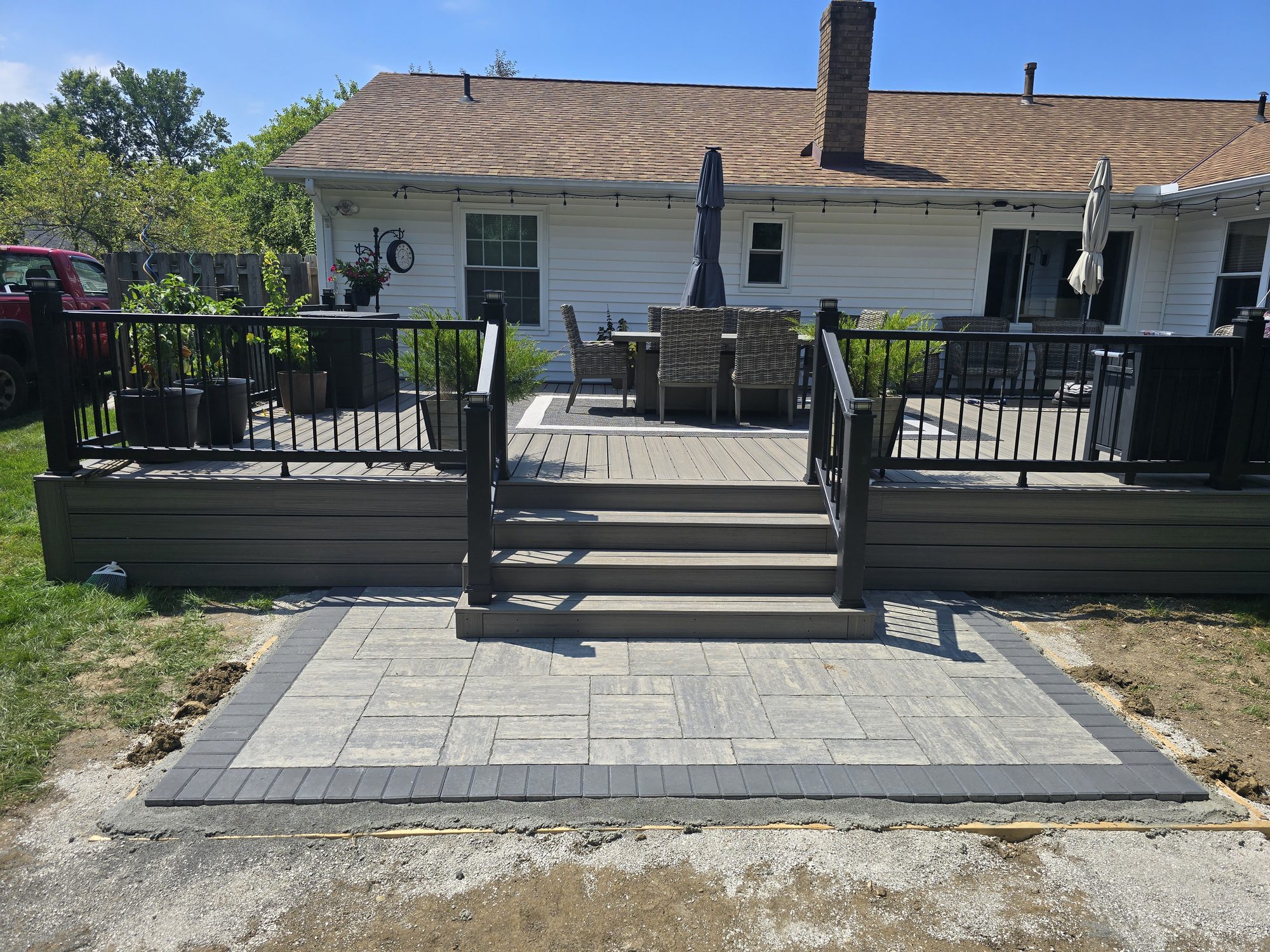 New paver patio installed at the base of a composite deck with a contrasting border course